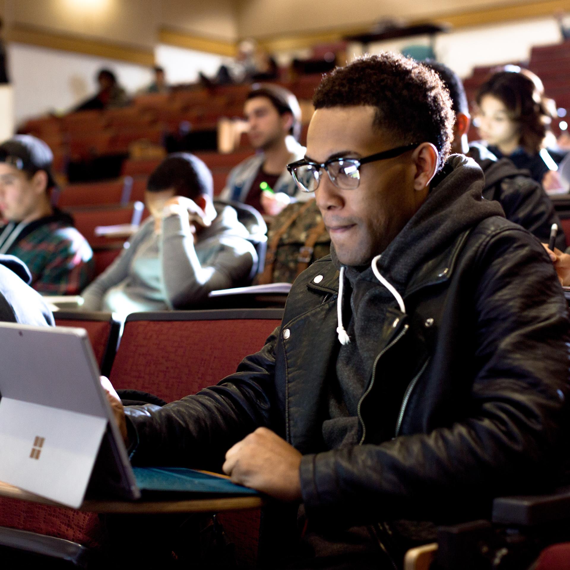 stock image of student with glasses in lecture hall looking at laptop